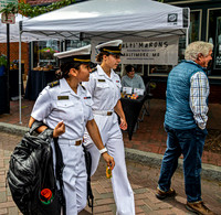 Two women in white uniforms walk past vendor's tent