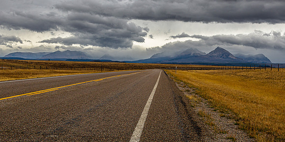 Empty Road Through Golden Field and Mountains