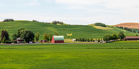 Crop duster over Palouse farmlands with barn.