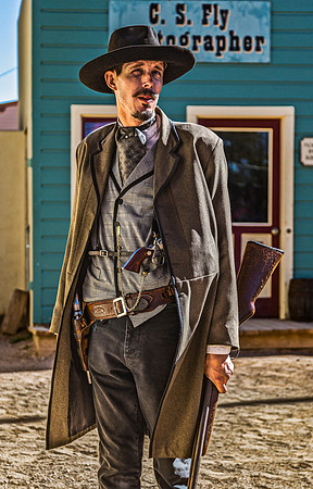 Man in cowboy outfit holding rifle and pistol.