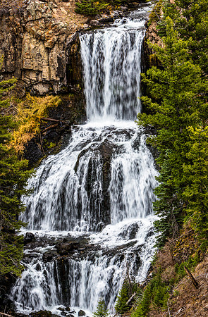 Cascading Waterfall Amidst Rocky Cliffs and Pine Trees